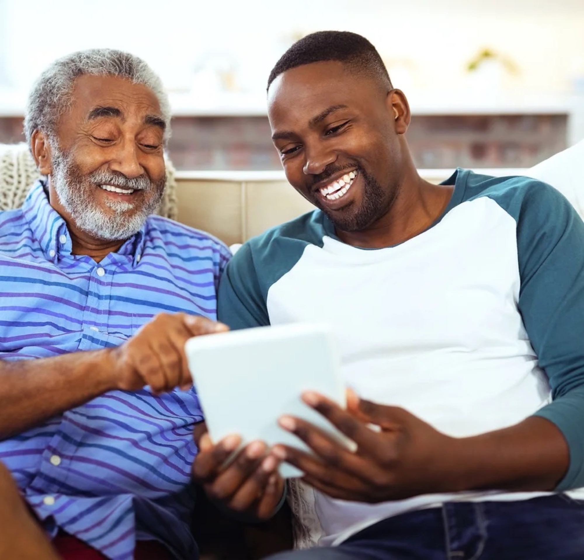 An older adult and a younger family member smiling while looking at a tablet together